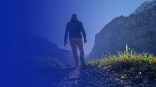 Back view of man walking along a grassy mountain ridge.