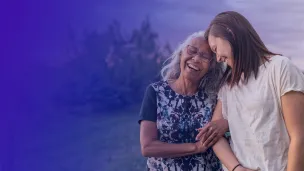 Smiling senior woman walking with younger woman arm in arm with sunset behind