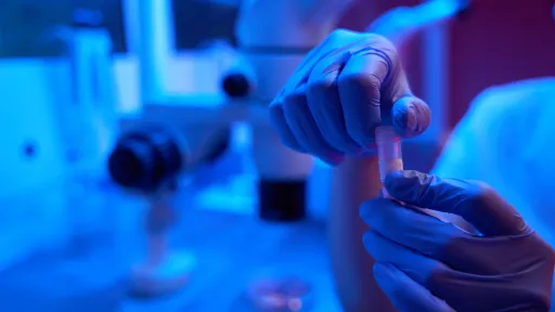 Laboratory professional holding a test tube in gloved hands.