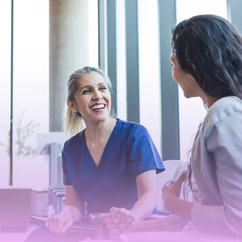 Female nurse holding patient's hand in supportive discussion during consultation.