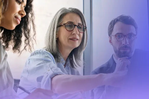 Three employees collaborating while looking at a computer screen in an office setting.